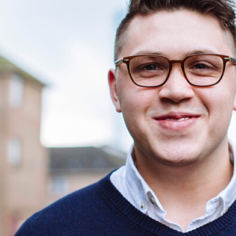 Male in blue jumper and glasses outside smiling at camera